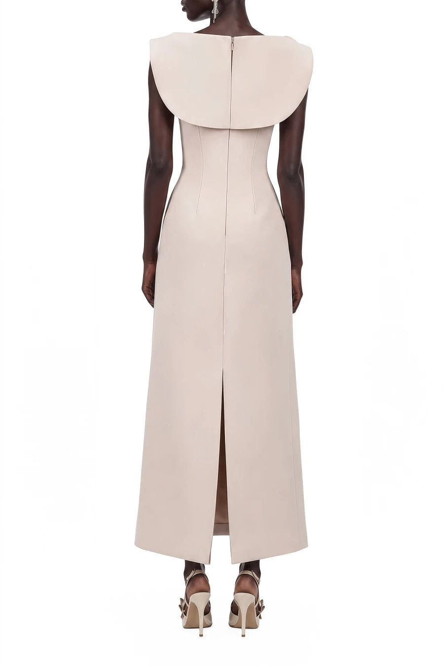 A model shown from the back wearing a sleeveless, floor-length beige dress with a dramatic oversized collar and a front slit, paired with brown high-heeled sandals against a plain white background.