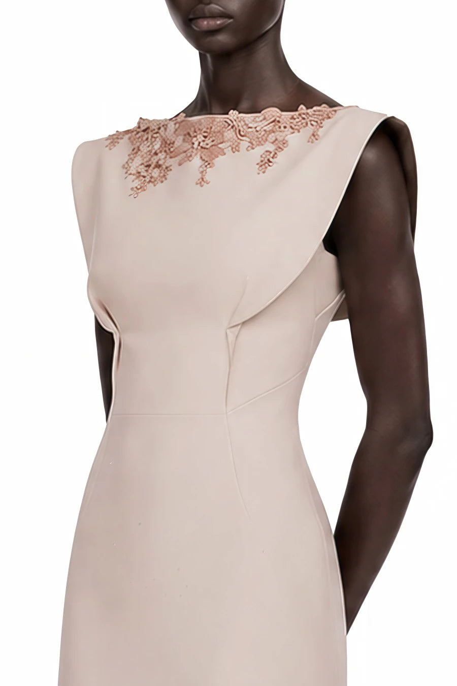 A sleeveless beige evening gown with a structured, draped neckline and rose gold floral lace embroidery across the shoulders, shown on a dark-skinned mannequin against a white background.