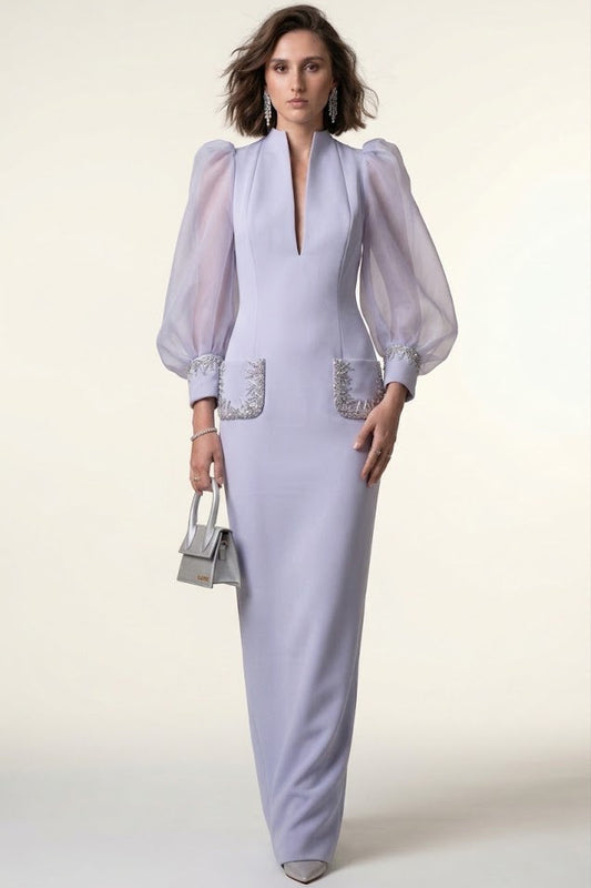 A woman models a lavender maxi dress with sheer balloon sleeves, a deep V-neckline, and silver embellished pocket details, holding a small silver handbag against a plain cream background.