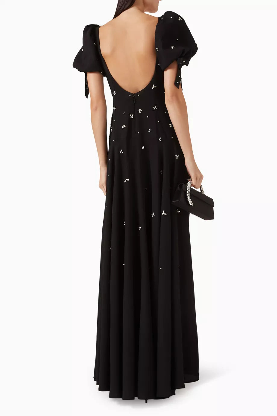 A black floor-length gown with a dramatic open back, short puff sleeves with tie details, and scattered silver floral embroidery, shown from the back on a model against a white studio background.