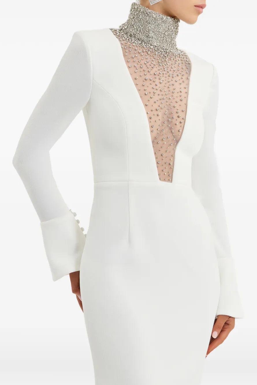 A model wearing a white long-sleeve gown with a high silver-beaded mock neck and a sheer embellished mesh panel at the plunging V-neckline.