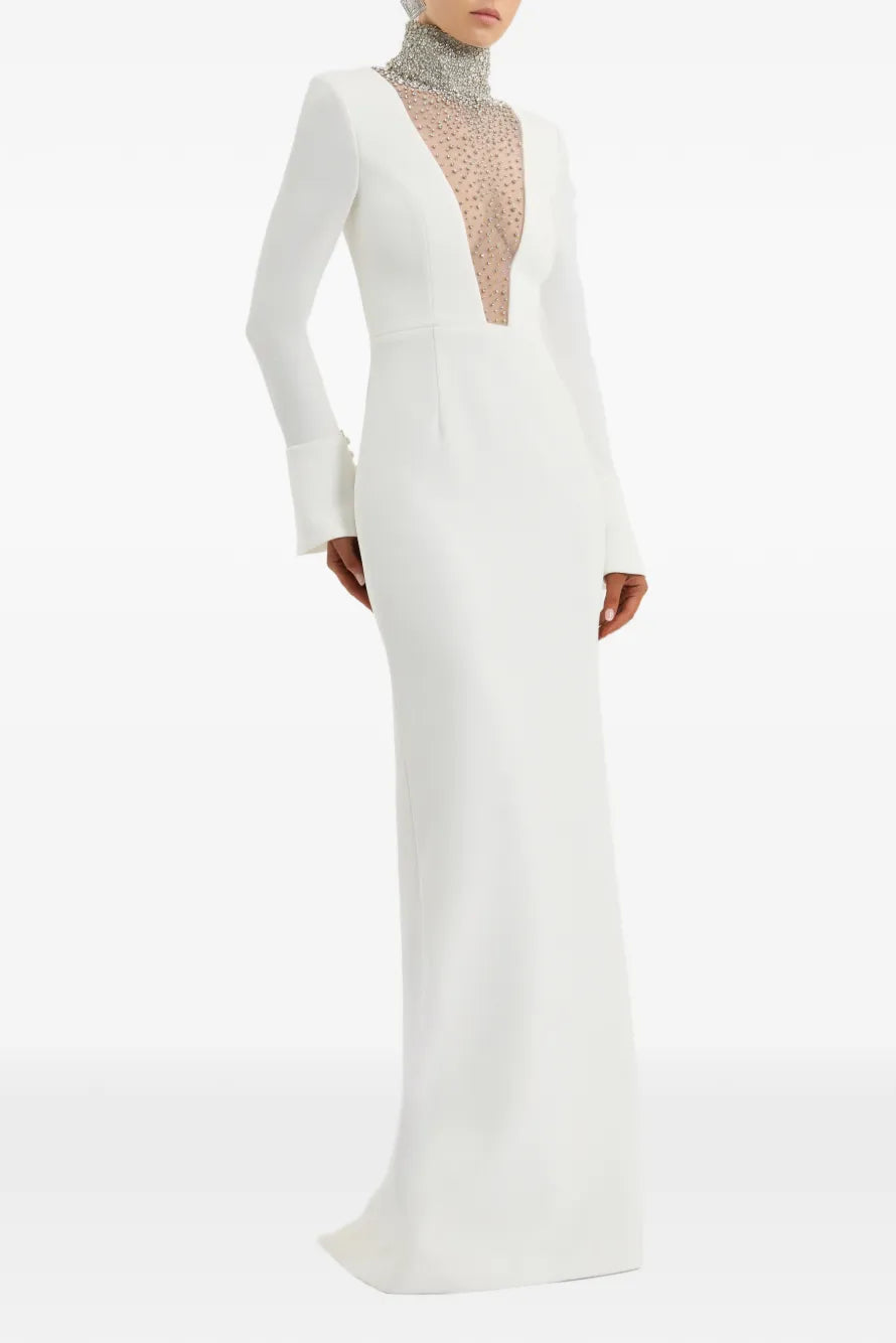 A floor-length white gown with long sleeves, a deep plunging neckline, and a sheer beaded mesh insert, shown on a model against a plain white background.