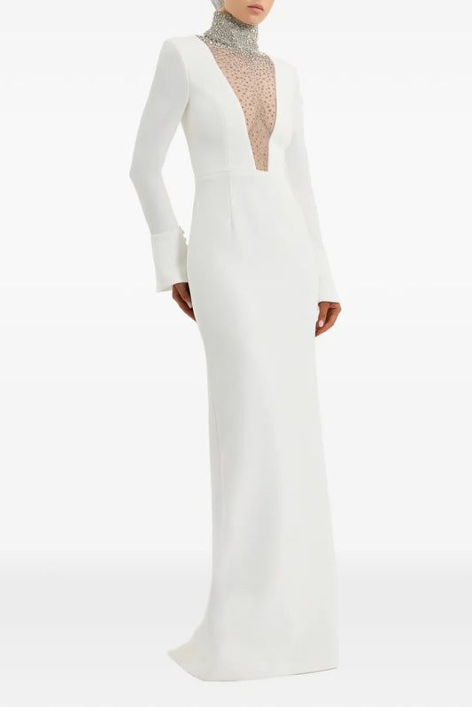 A floor-length white gown with long sleeves, a deep plunging neckline, and a sheer beaded mesh insert, shown on a model against a plain white background.