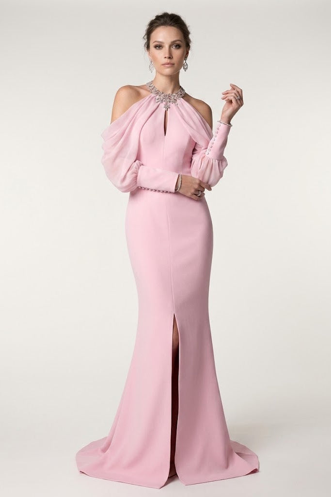 A woman models a floor-length light pink evening gown with a high neck, cold-shoulder puff sleeves, a fitted silhouette, and a front slit, photographed against a plain light beige studio background.