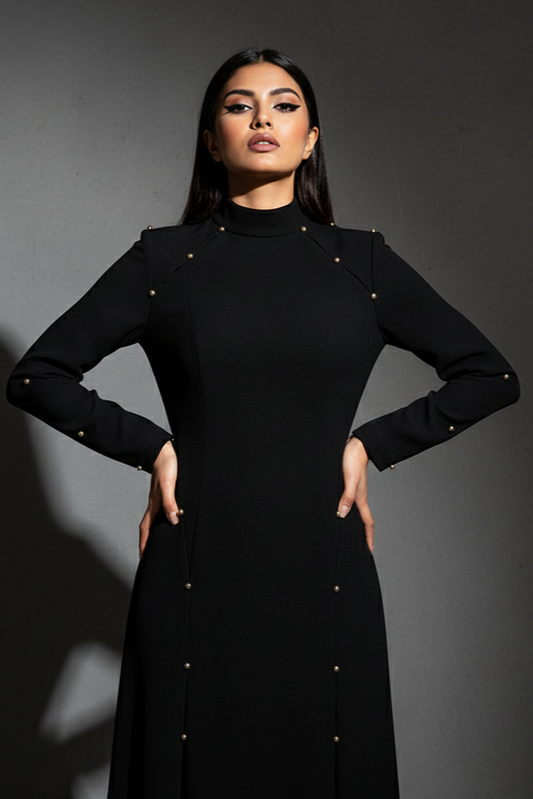 Woman wearing a black dress with gold buttons against a dark background