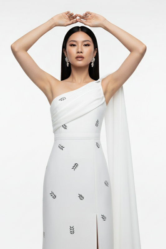 Woman wearing a white one-shoulder dress with black floral embroidery on a white background