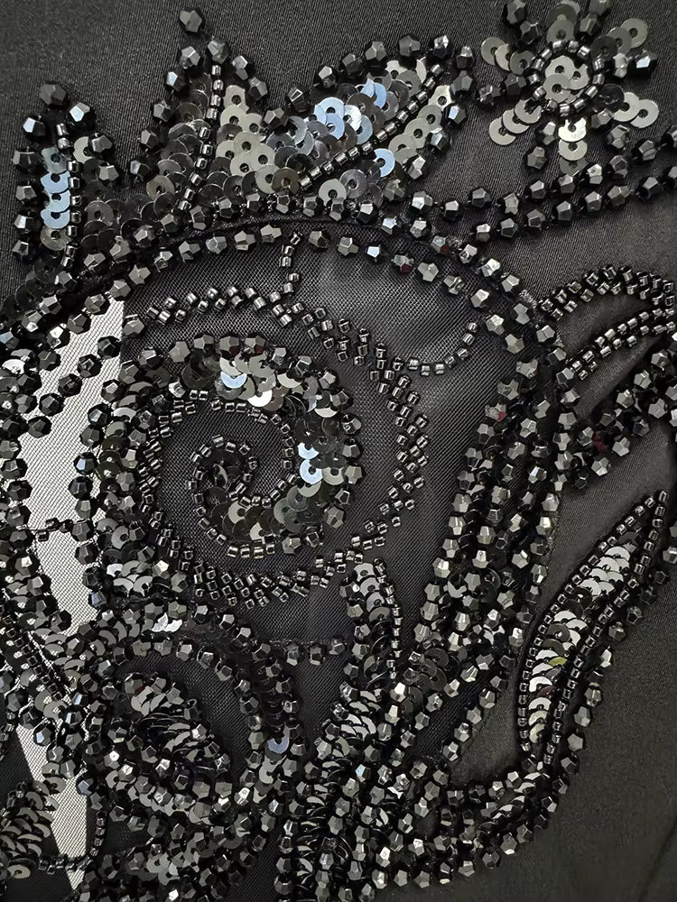 Close-up of a black sequin fabric with intricate patterns on a dark background