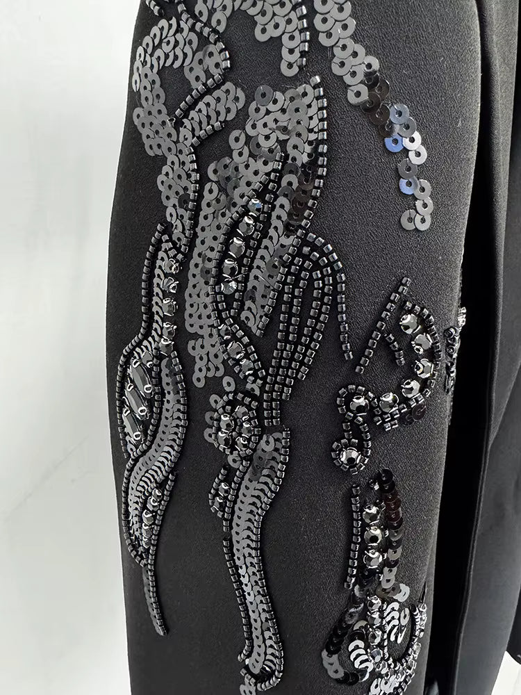 Close-up of a black garment with intricate silver sequin and bead detailing on a white background