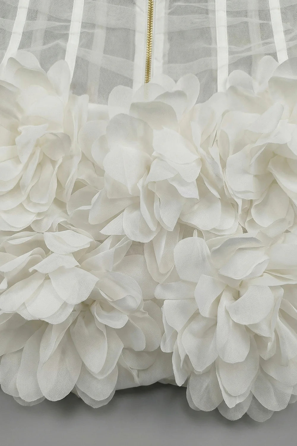 Close-up of a white floral dress with a sheer overlay on a light gray background