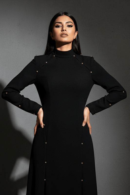 Elegant Modest Long Sleeve Black Evening Dress by Luxe Lane | from Luxe Lane | SKU:  | Barcode:  | Options: Black S | Woman wearing a black dress with gold buttons against a dark background