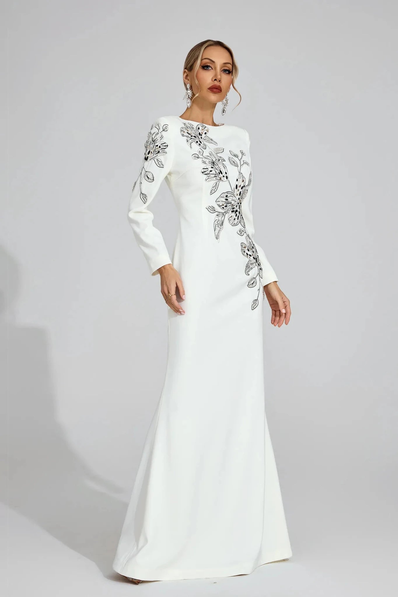Floral Embroidered Long Sleeve Mermaid Evening Gown by Luxe Lane | Party dresses from Luxe Lane | SKU: W11304-1 | Barcode:  | Options: White S(6) | Woman wearing a white evening gown with silver embellishments on a gray background