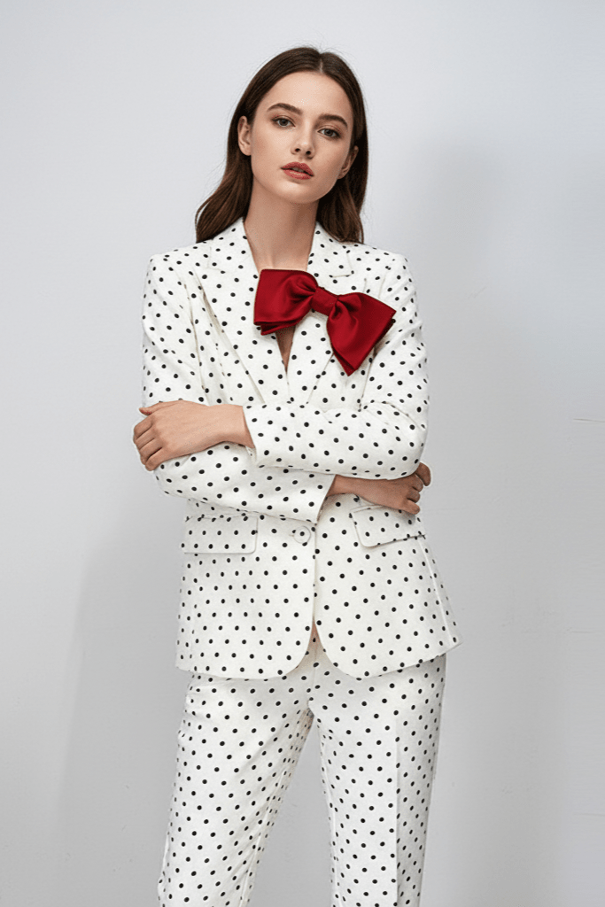 Polka Dot Blazer & Tailored Trouser Set with Red Bow Detail by Shine | Suits from Luxe Lane | SKU:  | Barcode:  | Options: Black S | Woman wearing a white polka dot suit with a red bow tie on a gray background
