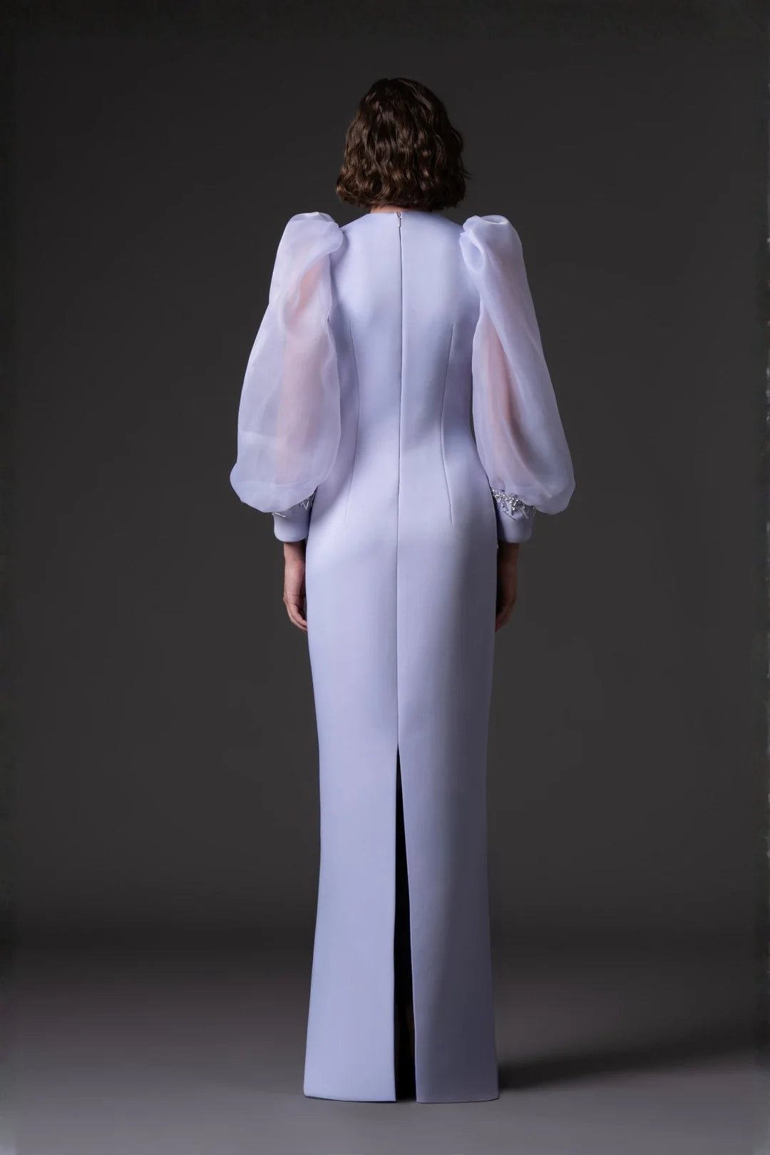 Person wearing a light gray dress with sheer sleeves against a dark background